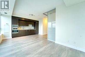 Toronto (Willowdale East) condo for rent - A spacious, empty room with wooden floors and a kitchen area in the background.