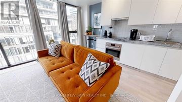Toronto (Waterfront Communities) condo for rent - A living room with a brown couch and a window overlooking a city.