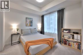 Waterloo condo for rent - A bedroom with a bed, a nightstand with a lamp, a bookshelf with books, and a painting on the wall.