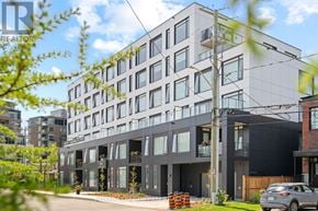 Ottawa apartment for rent - A modern building with a mix of grey and black exterior is surrounded by greenery and other buildings.