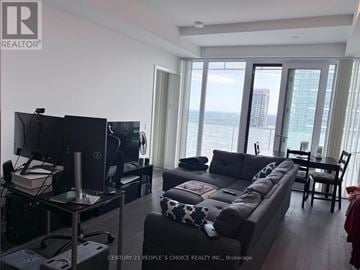 Mississauga (City Centre) condo for rent - A living room with a flat screen TV and a large window overlooking the water.