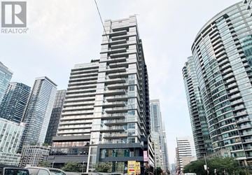 Toronto (Waterfront Communities) condo for rent - A tall building with a glass facade stands in front of other buildings.
