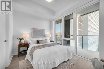 Toronto (University) condo for rent - A bedroom with a large bed and a view of a building outside the window.