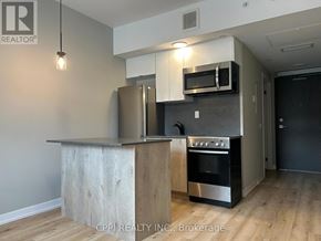 Oshawa (Central) condo for rent - A modern kitchen with a stainless steel refrigerator and microwave above a wooden island.