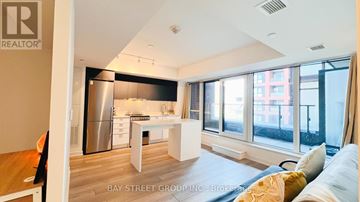 Toronto (Clanton Park) condo for rent - A well-lit, modern kitchen with a dining table and chairs, and a living area with a sofa and a window overlooking a city street.