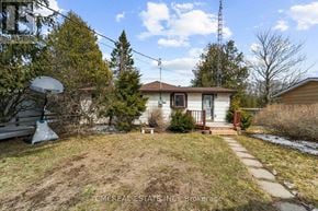 Trent Hills apartment for rent - A small house with a brown roof and a white door is surrounded by a grassy area and a few trees.