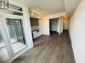 Toronto (South Parkdale) condo for rent - A spacious room with wooden flooring and white walls.