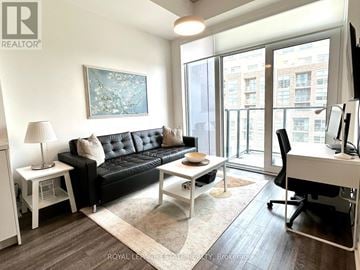 Toronto (Junction Area) condo for rent - A living room with a black couch, a white desk, and a painting on the wall.