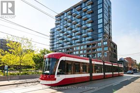 Toronto (South Parkdale) condo for rent - A red and white train is on the tracks in front of a tall building.