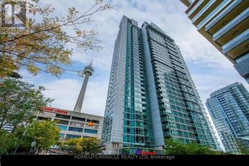 Toronto (Waterfront Communities) condo for rent - A tall building with many windows stands in front of a tree with autumn leaves.
