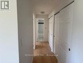 Oshawa (O'neill) multi-family for rent - A hallway with white walls and wooden floors leading to a door.