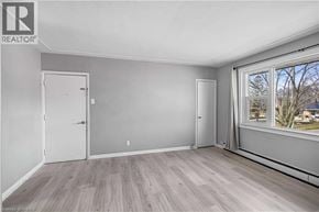Kitchener apartment for rent - A room with a white door, a window with a view of trees, and a wooden floor.