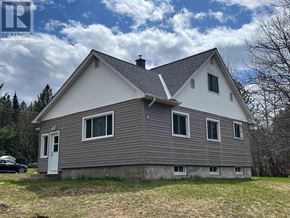 Richards Landing apartment for rent - A house with a grey roof and a white door is surrounded by grass and trees.