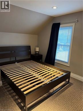 Brantford apartment for rent - A bed with wooden slats and a dark headboard sits in a room with a carpeted floor.