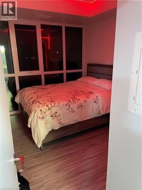 Waterloo condo for rent - A bedroom with a bed, wooden floors, and a window with red lighting.