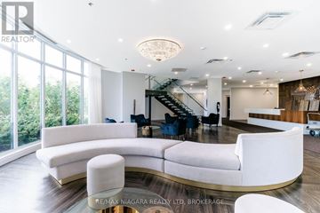 Niagara Falls (Oldfield) condo for rent - A modern living room with a curved white sofa and a staircase in the background.