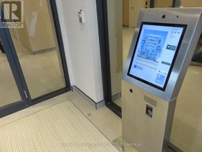 Brampton (Northwest Brampton) condo for rent - A digital kiosk with a screen displaying a map is situated in a hallway with a tiled floor and a glass door in the background.