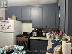 Ajax (Central West) multi-family for rent - A kitchen with a refrigerator, cabinets, and a table with various items on it.