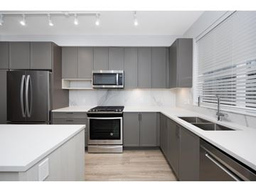 Surrey townhouse for rent - A modern kitchen with a refrigerator, oven, microwave, and sink.