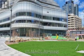 Toronto (Bay Street Corridor) condo for rent - A modern building with glass walls and a green lawn in front.