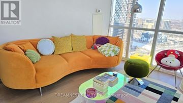 Mississauga (City Centre) condo for rent - A living room with a large orange couch and a view of the city.