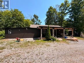 Trent Lakes apartment for rent - A house with a brown roof and a porch is surrounded by trees.