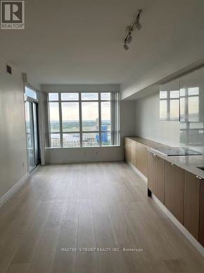 Toronto (Waterfront Communities) condo for rent - A spacious room with wooden flooring and a large window overlooking a cityscape.