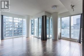 Toronto (Waterfront Communities) condo for rent - A spacious room with wooden floors and large windows overlooking a cityscape.