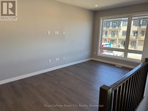 Guelph (Kortright East) townhouse for rent - A room with wooden flooring and a large window overlooking a city street.
