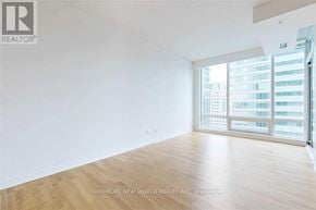Toronto (Waterfront Communities) condo for rent - A large, empty room with wooden floors and a view of a city skyline through the windows.