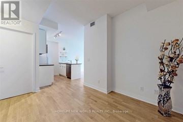 Toronto (Waterfront Communities) condo for rent - A spacious room with wooden flooring and white walls, featuring a kitchen area with white cabinets and a refrigerator.
