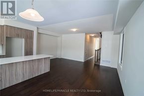 Barrie apartment for rent - A spacious room with wooden floors and white walls, featuring a large mirror and a hanging light fixture.