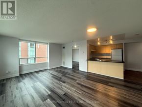 Markham (Commerce Valley) condo for rent - A large, empty room with wooden floors and a kitchen area in the background.