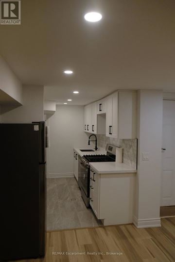 Toronto (Regent Park) townhouse for rent - A kitchen with a black refrigerator and white cabinets.