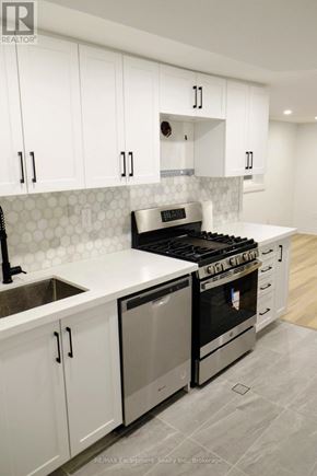 Toronto (Regent Park) townhouse for rent - A modern kitchen with white cabinets and a black stove top oven.
