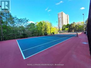 Toronto (Banbury-Don Mills) condo for rent - A tennis court with a red surface and white lines, surrounded by a fence and trees.