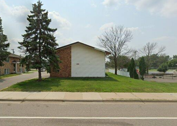 North Saint Paul apartment for rent - A small white building with a brick side and a grey roof sits in a grassy area.