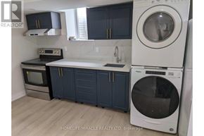 Brantford apartment for rent - A white washing machine is in a kitchen with dark blue cabinets.