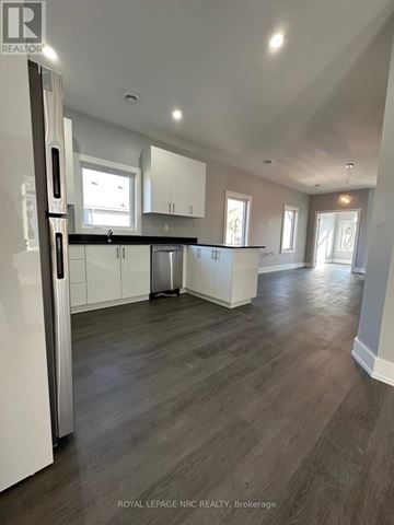 Welland (Welland Downtown) duplex for rent - A spacious kitchen with white cabinets and a dark wood floor.