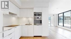Toronto (Bay Street Corridor) condo for rent - A modern kitchen with white cabinets and a wooden floor.