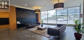 Mississauga (Central Erin Mills) condo for rent - A large, modern living room with a dark blue couch and a large window with a view of a parking lot.