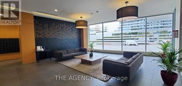 Mississauga (Central Erin Mills) condo for rent - A large, modern living room with a dark blue couch and a large window with a view of a parking lot.