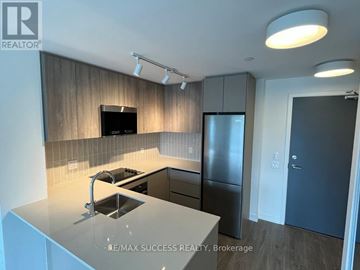 Mississauga (Central Erin Mills) condo for rent - A modern kitchen with a stainless steel refrigerator and a flat screen TV mounted above the cabinets.