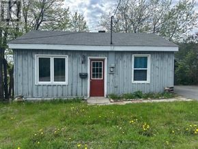 Parry Sound apartment for rent - A small blue house with a red door and windows surrounded by green grass and trees.