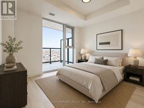 Burlington (Alton) condo for rent - A bedroom with a large bed, a nightstand, and a window overlooking a cityscape.