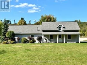 West Grey apartment for rent - A house with a grey roof and white walls is surrounded by green grass and trees.