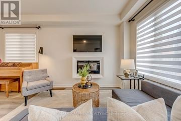 Hamilton (Waterdown) apartment for rent - A living room with a grey sofa, a grey armchair, a wooden table, and a television mounted on the wall.