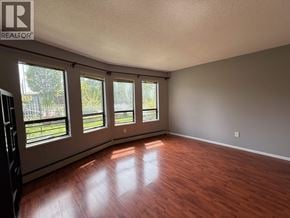 Vancouver apartment for rent - A room with wooden floors and a large window with a view of a fence and trees.