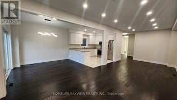 Innisfil (Lefroy) apartment for rent - A spacious room with wooden floors and white walls, featuring a kitchen area with white cabinets and appliances.
