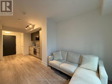 Toronto (Waterfront Communities) condo for rent - A living room with a white couch and a kitchen area in the background.